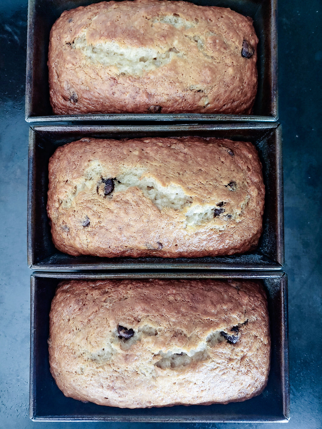 Three loaves of chocolate chip banana bread in baking trays.